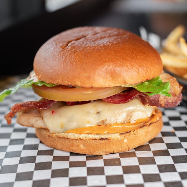 A chicken sandwich with melted cheese, bacon, tomato, and lettuce on a bun.