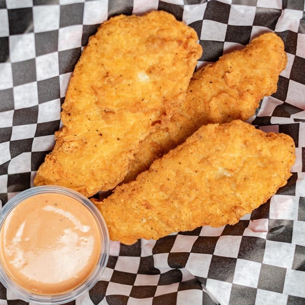 Three crispy fried chicken tenders and a cup of dipping sauce on black and white checkered paper.