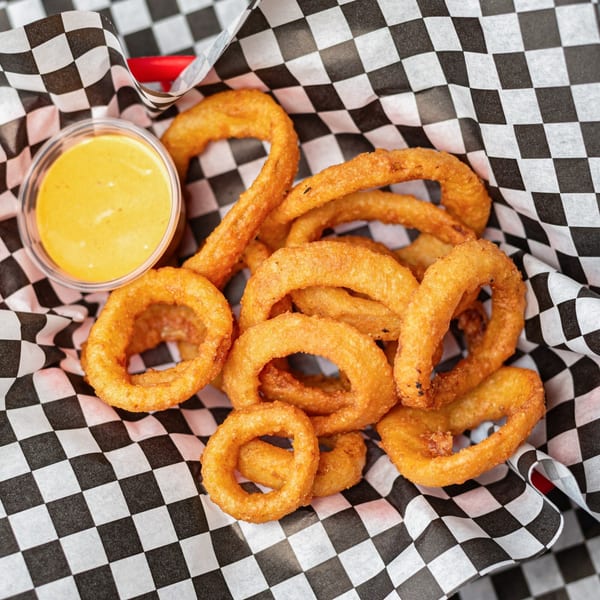 Golden-brown onion rings and a side of dipping sauce in a checkered paper-lined basket from Uncle Boy's.