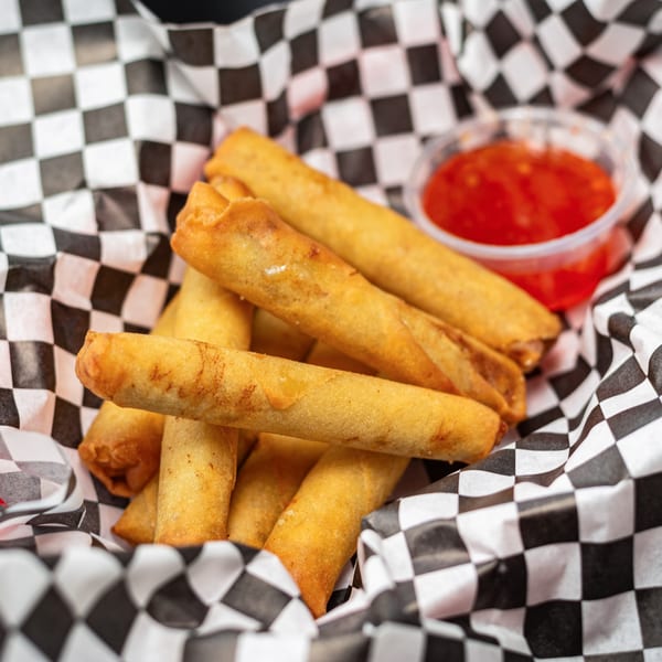 Golden-fried spring rolls in a checkered paper-lined basket with a side of sweet chili sauce.