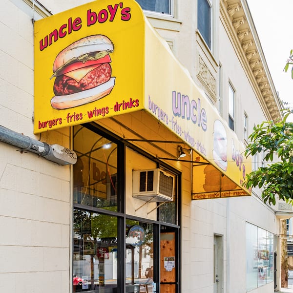 The exterior of Uncle Boy's burger restaurant, featuring a yellow awning with a burger illustration.