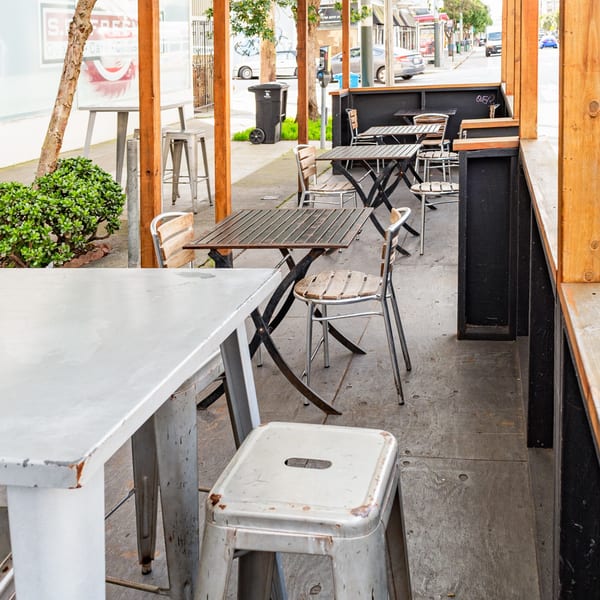 Outdoor patio seating area at Uncle Boy's with wooden tables and metal chairs under a wooden pergola.