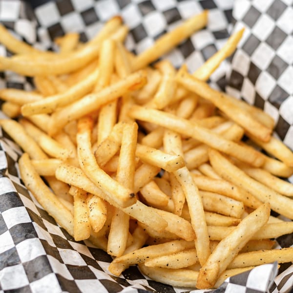 A close-up of golden, crispy French fries seasoned with pepper in a black and white checkered paper basket.