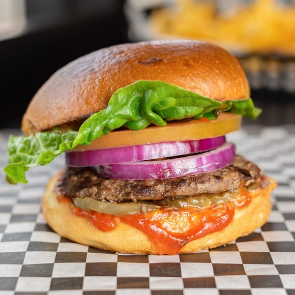 Uncle Boy's burger with lettuce, tomato, red onion, pickles, and sauce on a checkered wrapper.