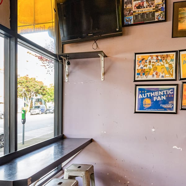 Interior of Uncle Boy's with window seating, a TV, and Golden State Warriors memorabilia on the wall.