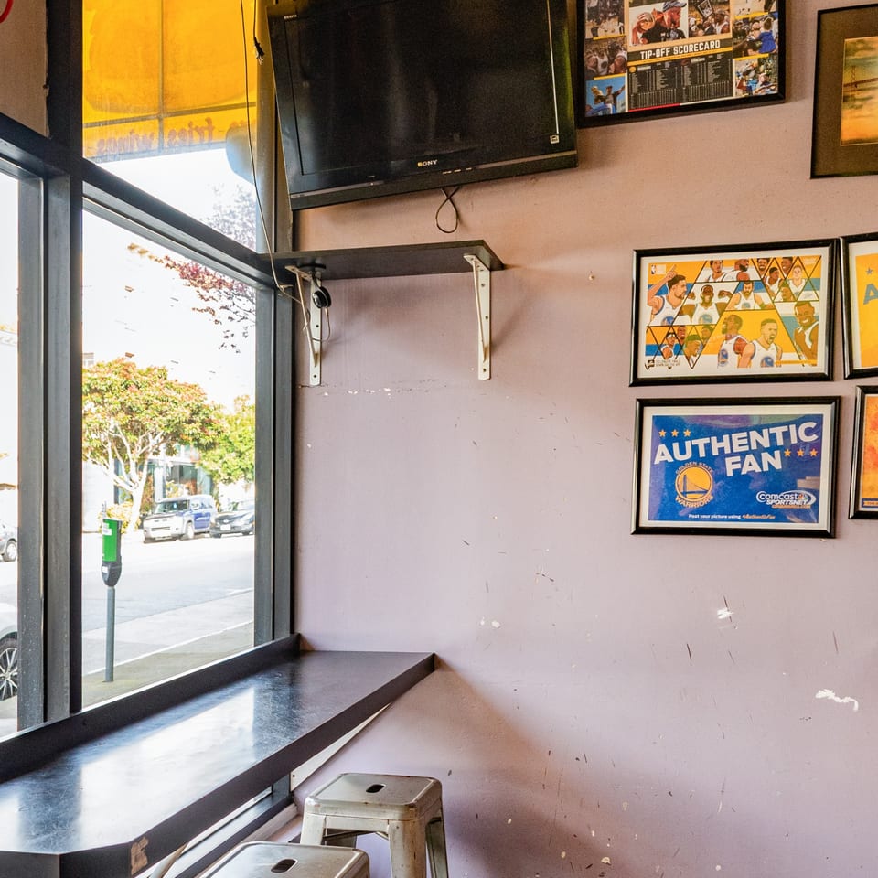 Interior of Uncle Boy's with window seating, a TV, and Golden State Warriors memorabilia on the wall.