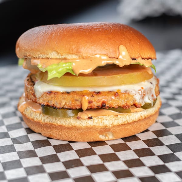 A close-up of an Uncle Boy's burger with melted cheese, lettuce, tomato, pickles, and sauce.