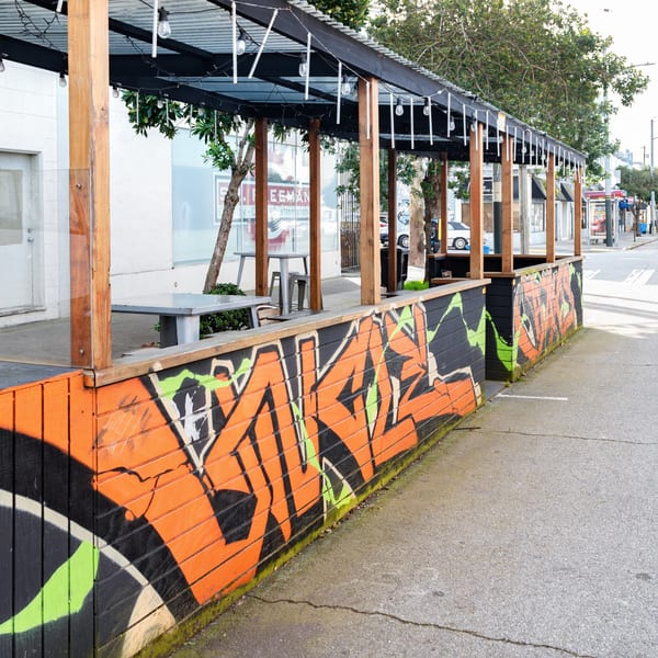 Outdoor dining patio with orange and black graffiti-style art on the walls, tables, and string lights.